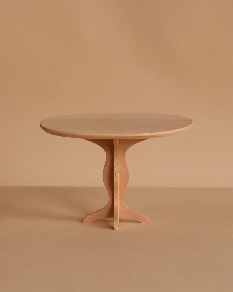 A small, round, wooden table with a simple design stands against a plain beige background. Ideal for showcasing the Maileg Ballet Bunny and Rabbit Set, it features a single central support with curved legs for a charming display.