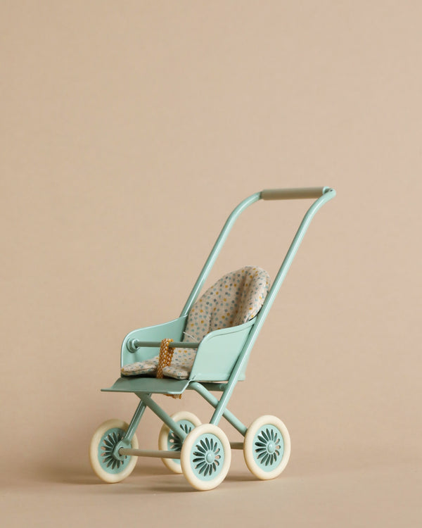 A Maileg Miniature Stroller in mint color with white wheels and beige padded seat, set against a plain light beige background.