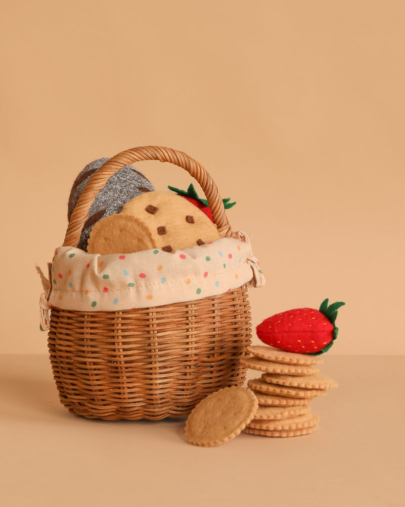 The Summer Picnic Basket Play Set features a rattan berry basket with a polka dot cloth liner holding felt cookies and a strawberry, with extra felt cookies stacked nearby on a beige background.