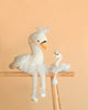 The Bukowski - Odette Ballerina Swan Set features two white plush swans in tutus and tiny hats, one large and one small, posed side by side on a wooden ladder against a peach background, resembling a parent and child.