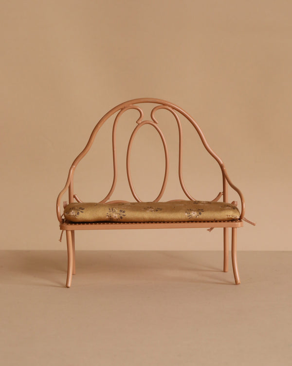 The Maileg Vintage Bench, Mini - Dark Powder, is a small ornate bench with a rounded backrest and armrests, painted dark powder pink and featuring a floral-patterned cushioned seat, set against a beige background.