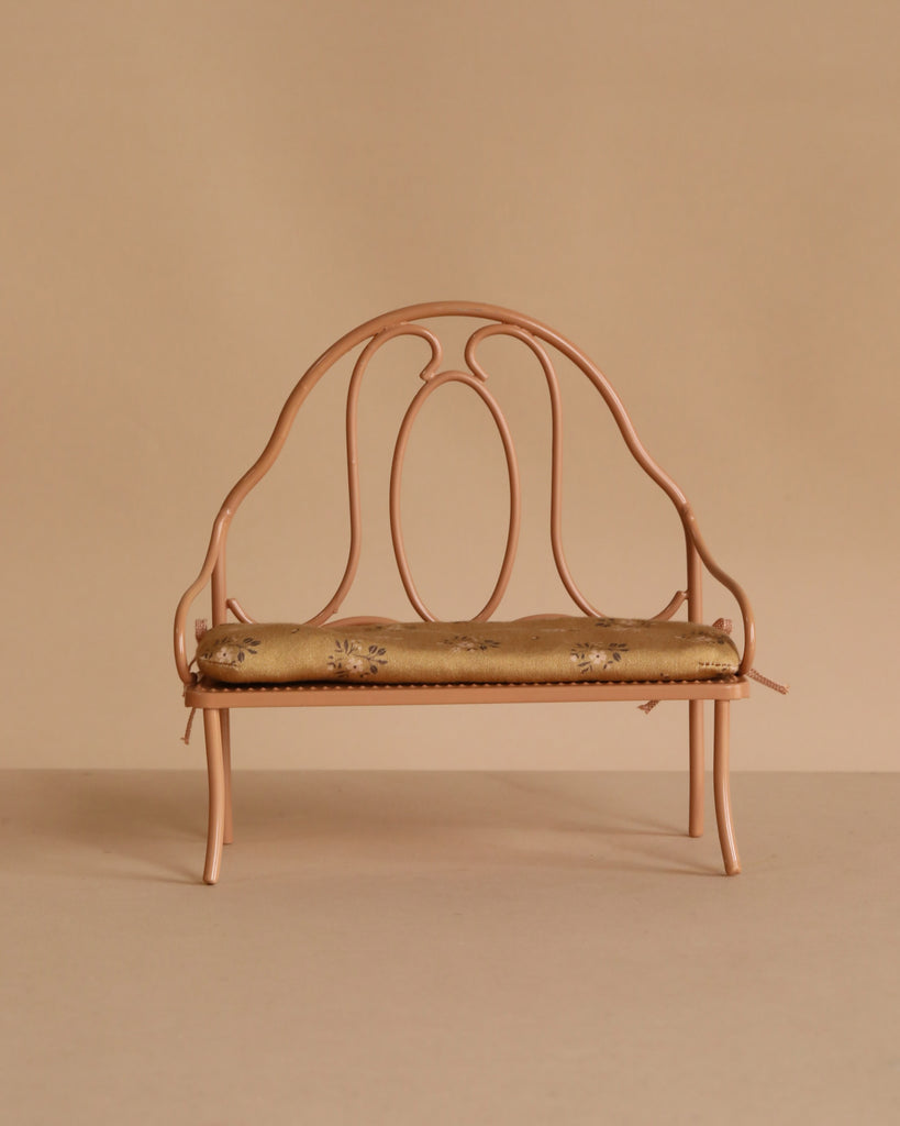 The Maileg Vintage Bench, Mini - Dark Powder, is a small ornate bench with a rounded backrest and armrests, painted dark powder pink and featuring a floral-patterned cushioned seat, set against a beige background.
