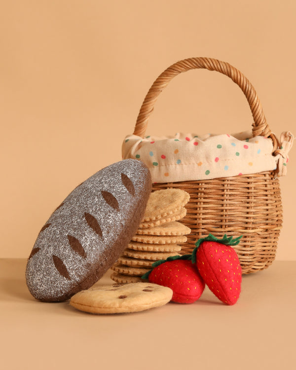 The Summer Picnic Basket Play Set features a small rattan basket with fabric lining, felt bread, round felt cookies, and two red strawberries, all displayed on a beige background.
