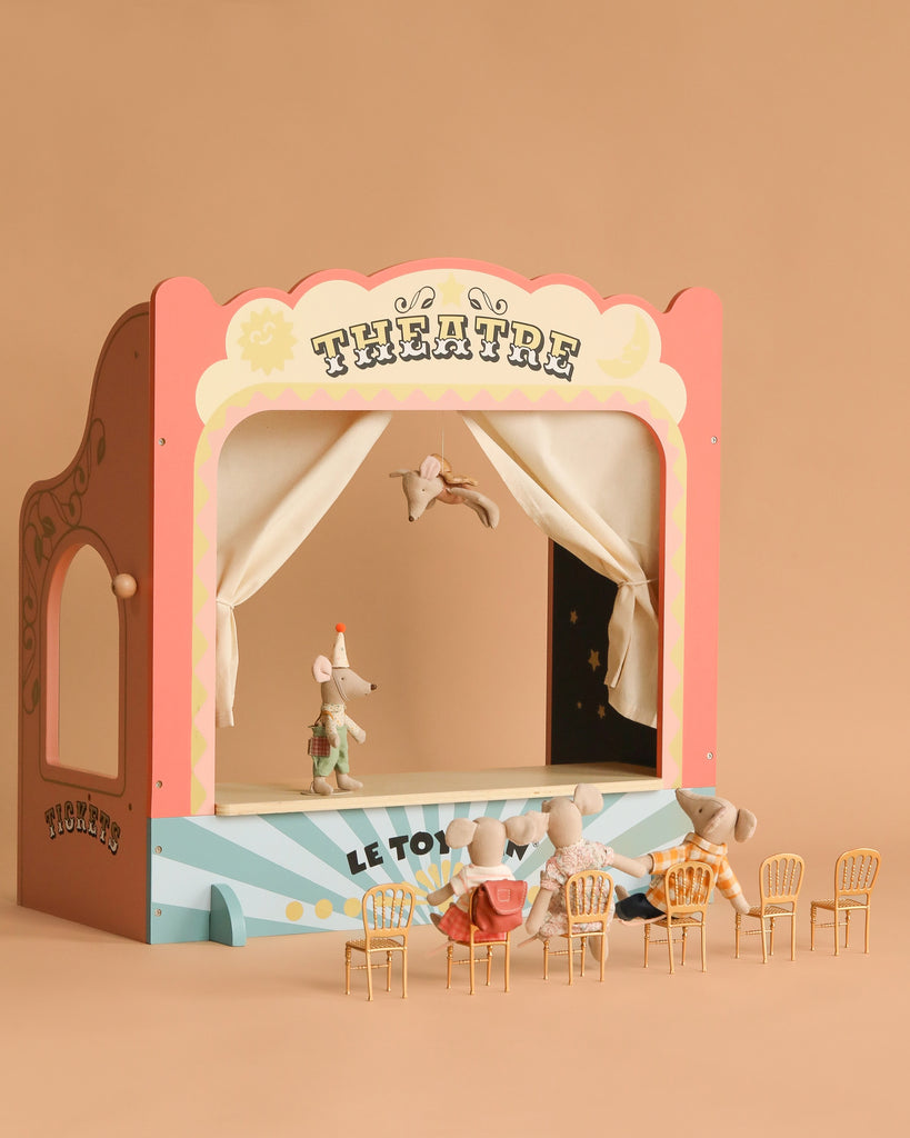 The Maileg Family Theater Set creates a magical scene with tiny mice—one performing on stage, an acrobat above, and four seated on Maileg dollhouse furniture. The beige background enhances this enchanting toy theater display.