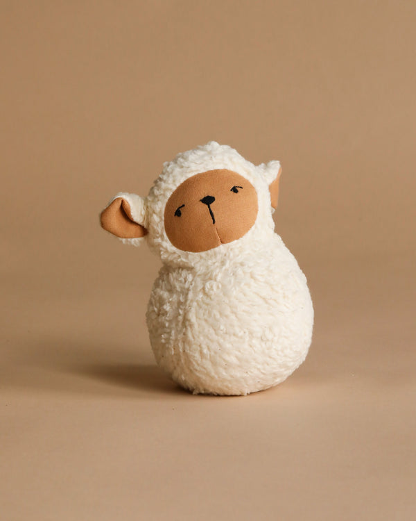 The Organic Cotton Sheep Tumbler features a soft, white textured body, beige face, and floppy ears. Sitting upright on a beige background, it's ideal for sensory exploration and developing gross motor skills.