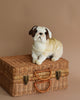 A Bulldog Stuffed Animal, part of the HANSA animals collection, sits on top of a woven wicker suitcase against a plain beige background. The bulldog has a white body with brown patches around its eyes.