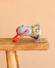 The Moulin Roty Storybook Lantern - The Minouchkas, a vibrant toy projector with a red handle and two round image reels, sits on a wooden surface against a plain beige background.