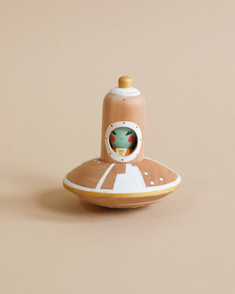 A whimsical Handmade Wooden UFO With Alien, crafted in shades of beige, white, and green, with a natural wood finish, against a plain beige background.
