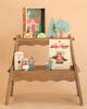 The Your Story of Little Red Riding Hood display features a plywood box shelf with paper cutout characters, trees, a house, and a storybook, all arranged as a woodland scene toy on two shelves against a peach background.