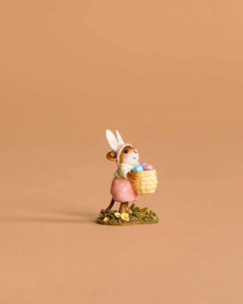 The Wee Forest Folk Tiny Collectible - Hoppy Easter Girl (Not a Toy) features a handmade mouse in a pink dress with bunny ears, holding a basket of pastel eggs on grass—a delightful piece for collectors.