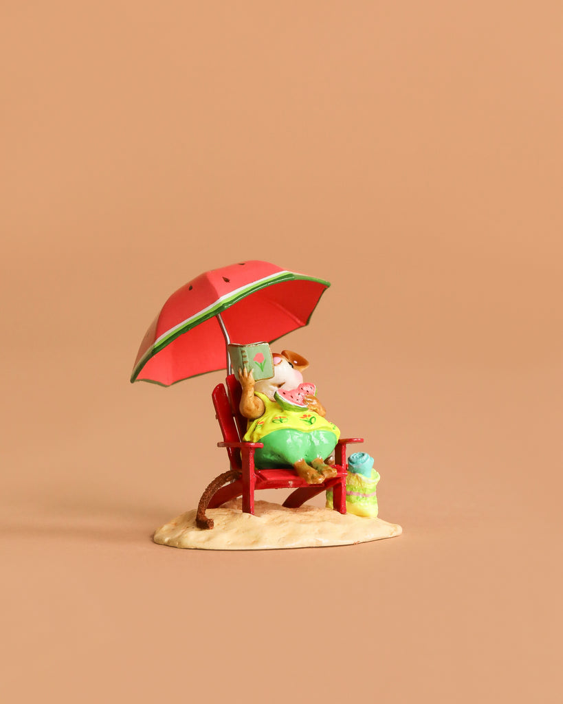 The Wee Forest Folk Tiny Collectible - Perfect Beach Day! features a hand sculpted mouse lounging on a red beach chair under an umbrella, reading with a drink on the sand, set against a plain light brown background.