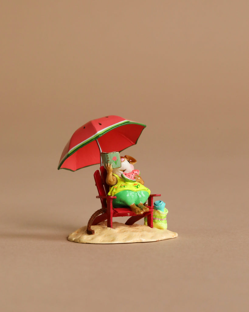 The Wee Forest Folk Tiny Collectible - Perfect Beach Day! shows a figure in green clothes relaxing on a red chair under a red umbrella, reading by a blue bag on sand, all set against a plain beige background.