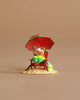 The Wee Forest Folk Tiny Collectible - Perfect Beach Day! features a hand-sculpted mouse in green shorts relaxing on a red chair under a matching umbrella, holding watermelon and a book, with tiny accessories on sandy ground.