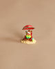 A hand-sculpted mouse lounges on a beach chair under a red umbrella, with a green table, drink, and bag on sand—a Wee Forest Folk Tiny Collectible: Perfect Beach Day! (Not a Toy), set against a plain beige background.