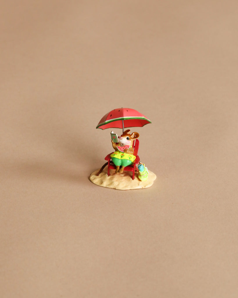 A hand-sculpted mouse lounges on a beach chair under a red umbrella, with a green table, drink, and bag on sand—a Wee Forest Folk Tiny Collectible: Perfect Beach Day! (Not a Toy), set against a plain beige background.