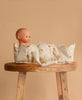 A Konges Sloejd Doll Lift - Lemon, made from soft, OEKO-TEX certified white fabric with small yellow lemon designs, holds a baby doll sitting on a rustic wooden stool against a plain beige background.
