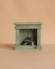 The Maileg Grand Dining Room Set includes a small, green, rectangular model fireplace with stacked logs for a Mouse Size dollhouse, shown against a plain beige background.