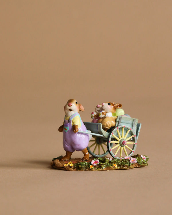 The Wee Forest Folk Tiny Collectible - Easter's on its Way features a small mouse in purple overalls pulling a blue cart with two companions, all hand-sculpted miniatures on a flower-decorated base.