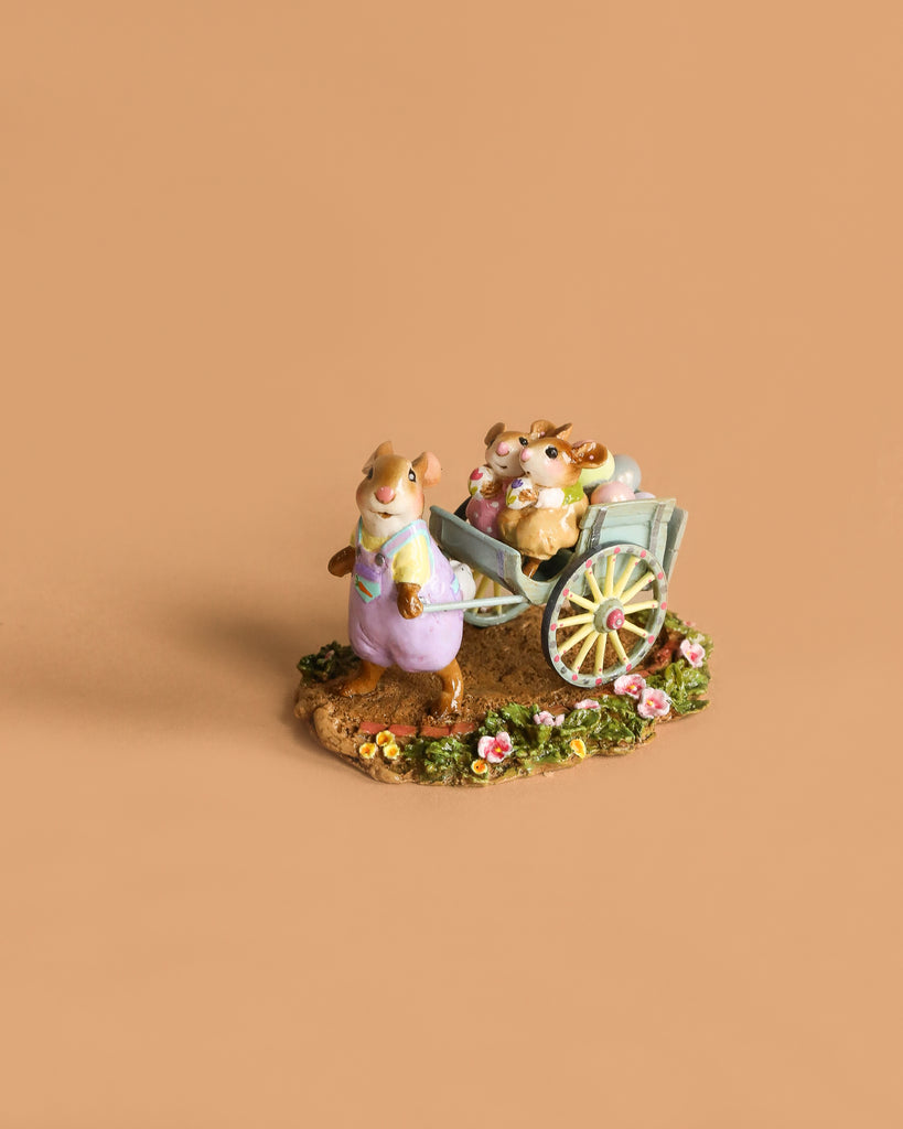 The Wee Forest Folk Tiny Collectible, "Easter's on its Way," features a ceramic rabbit in purple overalls pulling a cart with a smaller rabbit and pastel eggs on a flower-adorned base, set against a plain beige background.