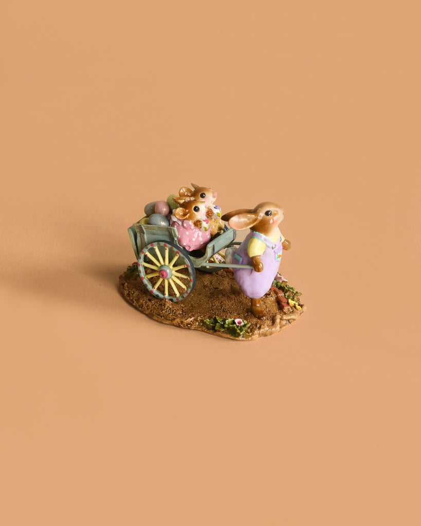 The Wee Forest Folk Tiny Collectible - Easter's on its Way features a rabbit in purple overalls pulling a cart of pastel eggs and another bunny, set on a textured green and yellow base.