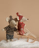 The Maileg Winter Mouse with Ski Set, Big Sister - Rose, features two charming mice adorned in cozy winter attire. One is positioned on a wooden sled crafted from recycled polyester, while the other stands nearby. Both are decked out in knitted hats and sweaters, set against artificial snow with a beige backdrop.