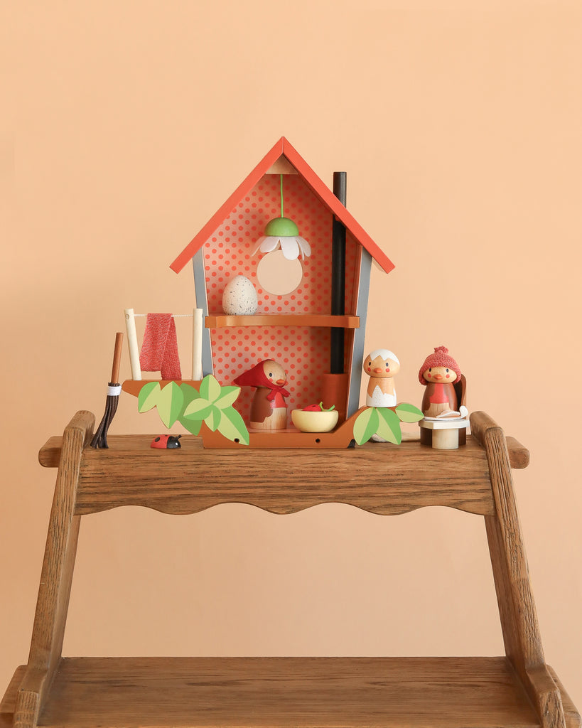 The Robin's Nest Box is a small wooden shelf featuring a decorative birdhouse, egg-shaped ornaments, a red bird and duck figurine, a doll in a red hat, toy leaves, and household miniatures—ideal for imaginative play against a peach background.