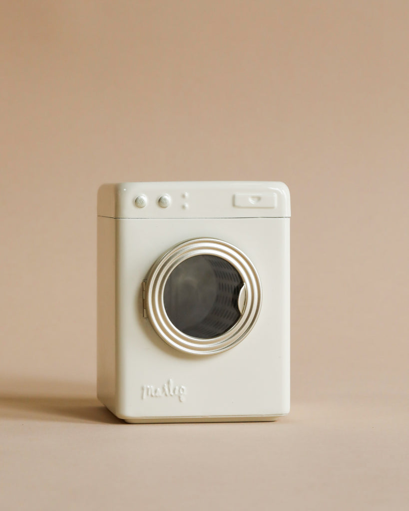 A compact, white Maileg Washing Machine with a prominent round lens and simplistic design, against a soft beige background.