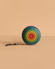 The Mader Wooden Yoyo - Rainbow features handcrafted concentric rainbow circles and a black string, resting on a beige surface. This vibrant, non-toxic toy offers a playful option for kids and collectors alike.