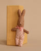 A Maileg My Rabbit - Dots, a plush brown bunny adorned with a pink bow and polka-dotted details, is propped against a wooden block against a neutral backdrop.