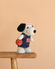 Peanuts Snoopy - Basketball plush, featuring Snoopy in a basketball jersey and headband, holding a basketball while standing on a wooden bench against a plain beige background.