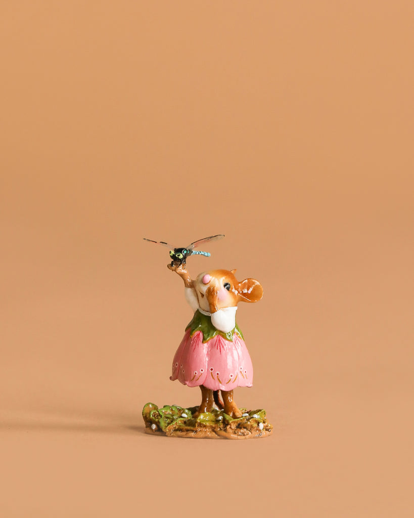 The Wee Forest Folk Tiny Collectible - Pretty Perch in Pink features a hand sculpted mouse in a pink dress standing on grass and holding a dragonfly, set against a plain light brown background.