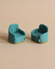 Two miniature teal armchairs, perfect for a Maileg Living Room Starter Set, with tags, set against a plain beige background. Each chair has a decorative yellow stitch along the bottom edge.