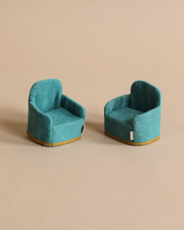 Two small size teal color chairs photographed against beige background. 