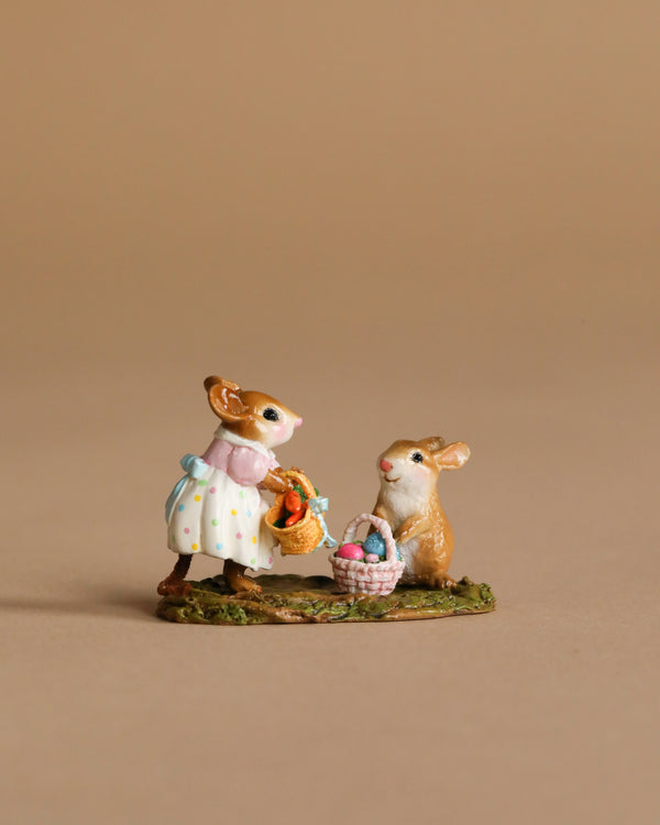 On display is the Wee Forest Folk Tiny Collectible - Baskets Full of Easter Joy (Not a Toy), featuring two handmade mouse figurines: one in a dress with flowers, the other beside a basket of colorful eggs, set against a plain beige background.