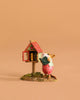 The Wee Forest Folk Tiny Collectible - Little Library in Pink features a mouse in a pink dress holding a blue book beside a red-roofed outdoor bookshelf, set against a beige background.