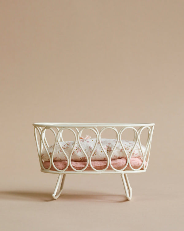 A white wire rack holding four Maileg Miniature Cradles with pink sand on a beige background, suggesting a minimalist and elegant design.