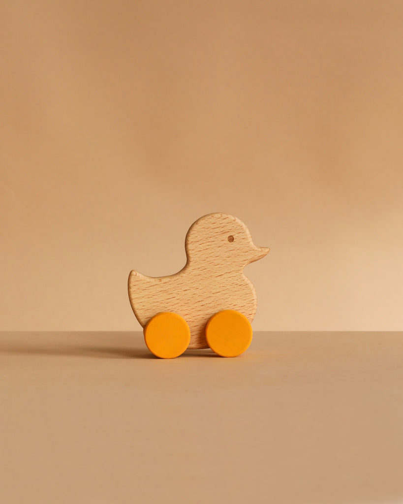 A wooden duck-shaped toy with two yellow wheels sits on a flat surface against a light brown background, ready to be tucked into the Easter Basket Gift Set for an Easter Egg hunt or added to a Handmade Explore Basket.