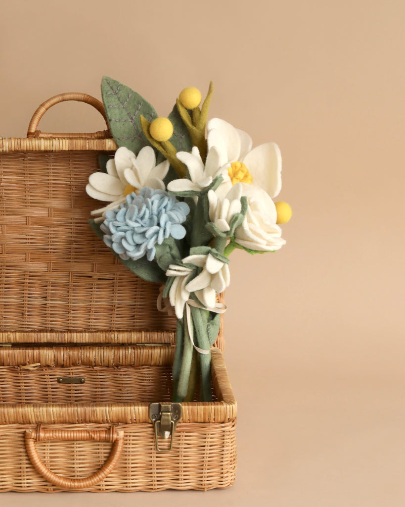 A stack of two closed wicker picnic baskets with a Felt Flower Bouquet - Butterfly Bliss protruding from the top basket's handle, against a beige background. These eco-friendly baskets are perfect for outdoor gatherings.