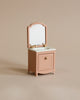 The Maileg Bonus Room Bathroom Set features a small, vintage-style pink vanity with a mirror, gold faucets, and a single cabinet door—perfect for enhancing any miniature dollhouse accessories collection. Set on a plain beige background.