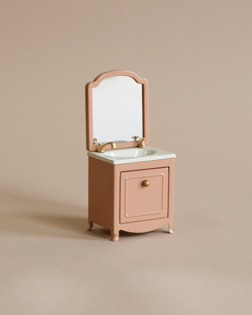 A Maileg Miniature Sink with Mirror in pink, with a single drawer and golden accents on a neutral background.