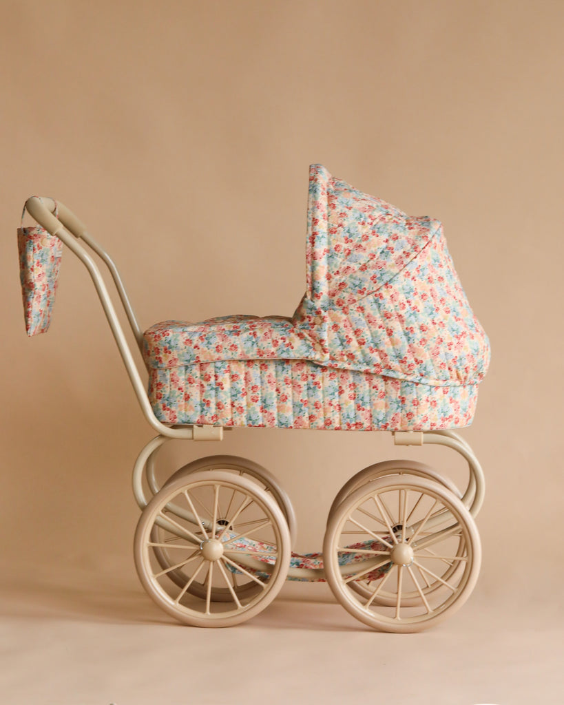 The Konges Sloejd Mini Doll Pram - Vienna features a cream frame, large spoked wheels, and floral fabric in pink, blue, and green on beige—perfect for play or display.