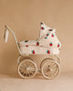 The Konges Sloejd Mini Doll Pram - Strawberry features a vintage style with large wheels and quilted fabric decorated with a red and green strawberry pattern on a beige background.
