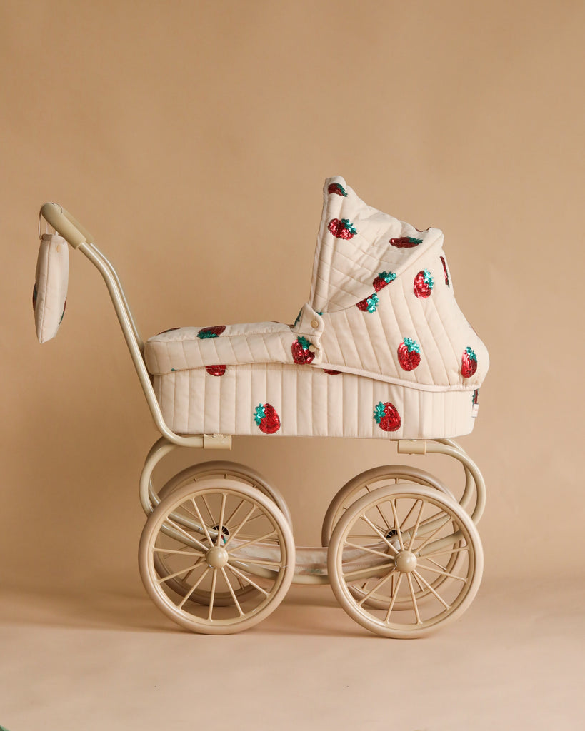 The Konges Sloejd Mini Doll Pram - Strawberry features a vintage style with large wheels and quilted fabric decorated with a red and green strawberry pattern on a beige background.
