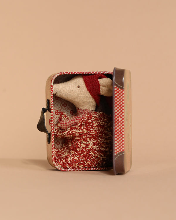 The Maileg Christmas Mouse, Baby in Suitcase, is dressed in a red knitted sweater and hat, snugly nestled in an open small travel suitcase against a beige background.