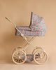 The Konges Sloejd Doll Pram - Kyoto features floral-patterned quilted fabric, a cream-colored metal frame, padded mattress, and large spoked wheels, beautifully set against a beige background.