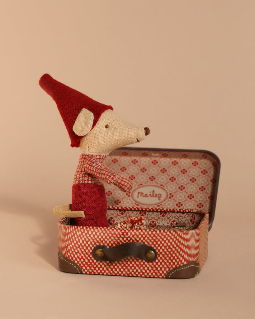 Inside an open, patterned travel suitcase against a neutral background lies the Maileg Christmas Mouse, Baby, dressed in a red outfit and hat.