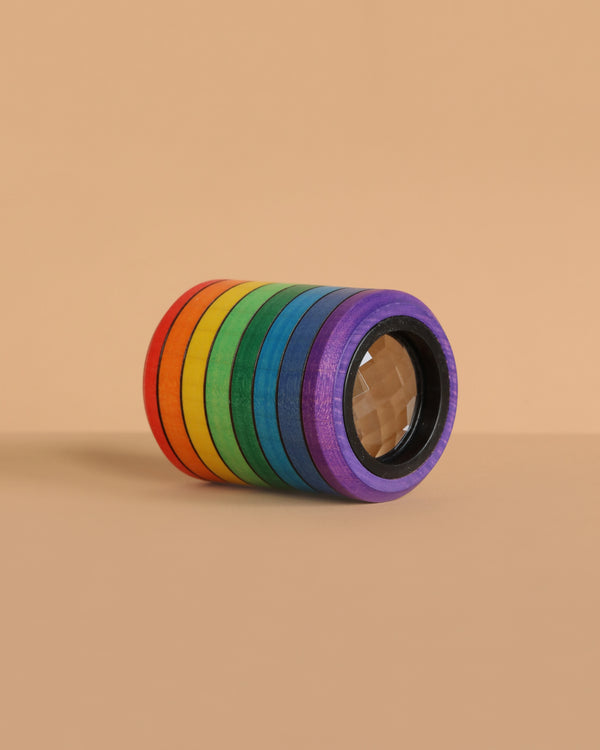 The Mader Rainbow Kaleidoscope, featuring adhesive tape rolls in red, orange, yellow, green, blue, and purple, is stacked on a beige surface and background for a vibrant display reminiscent of a kaleidoscope lens.