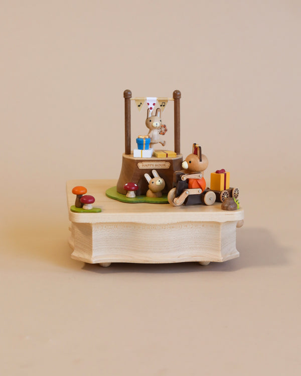 A whimsical miniature scene featuring a small Wooden Bunny Music Box celebrating a birthday with a cake and gifts on a tiny wooden table, crafted from sustainably sourced wood, set against a neutral background.