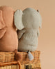 Sentence with Product Name: Two Maileg Small Elephant toys, one gray and one brown, sitting on a wicker basket with a soft beige background. Both safari friends have their backs to the viewer, displaying large floppy ears and tiny tails.