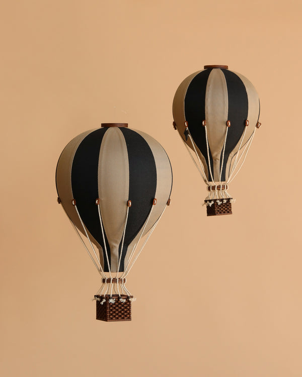Two vintage-style Hot Air Balloon - Black models with black and beige stripes and small woven baskets float against a plain beige background—ideal as unique children's room decor.